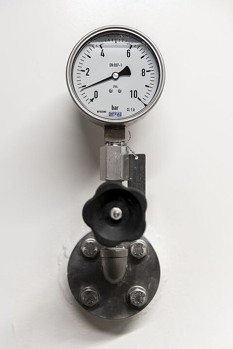 Manometer zur Druckmessung, montiert an einer Metallleitung. Das Ziffernblatt zeigt Werte im Bereich von 0 bis 2 bar an. Eine schwarze Handradventilöffnung ist unterhalb des Manometers sichtbar.