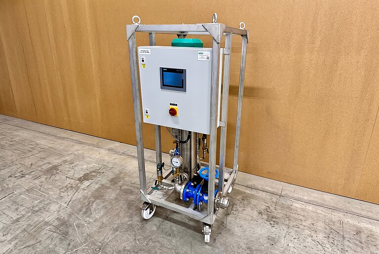 Ein industrielles Gerät auf einem stabilen Rahmen mit einem Touchscreen-Display, Knöpfen und verschiedenen Rohren und Ventilen. Es steht auf Rollen und ist für technische Anwendungen in einer Werkstatt oder Fabrikumgebung konzipiert. Der Hintergrund ist eine helle Wand.