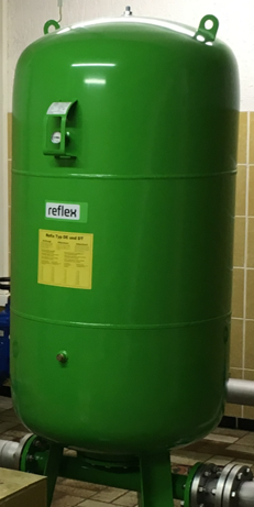 Ein großer, grüner Drucktank mit der Aufschrift "reflex" und einer Informationskarte auf der Vorderseite. Der Tank steht auf einem Boden aus Fliesen und ist mit Rohrleitungen verbunden.